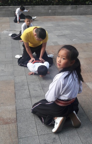 Gewoon op straat, in Guangzhou. Kinderen met kleding waarop tekens staan die 'Shaolin' betekenen worden met ietwat harde hand soepel gemaakt. Niet ieder kind kan daar tegen.